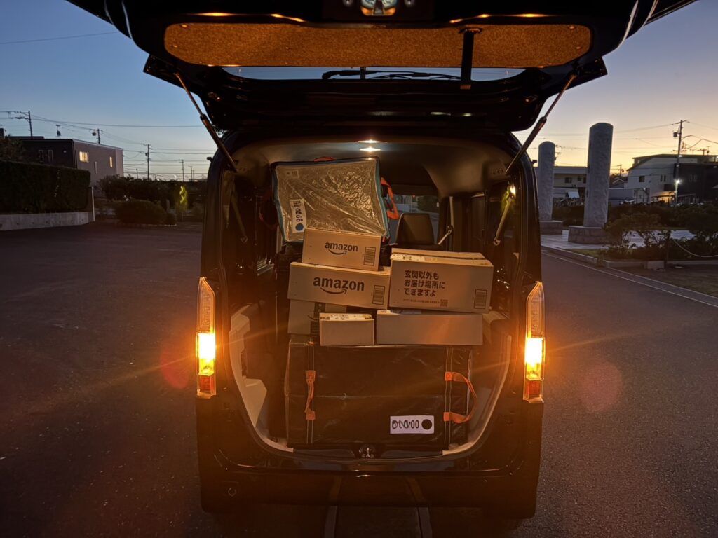 夜の道路でリアゲートを開けたN-VAN e:。荷室に積まれたAmazonの段ボールがライトに照らされている。